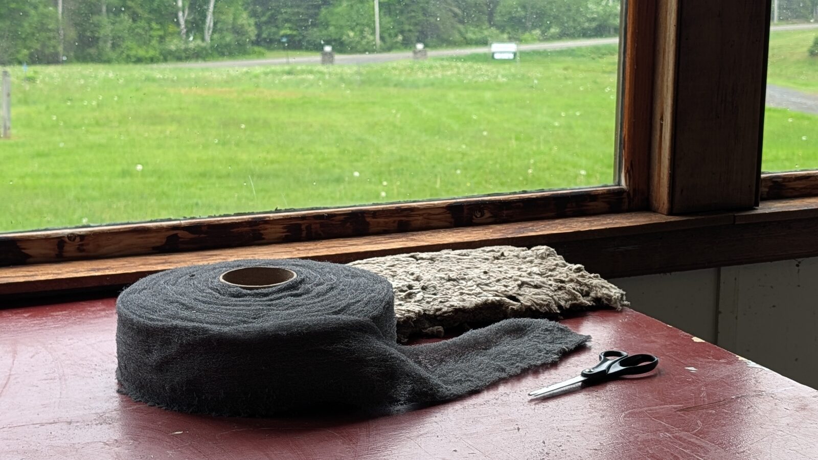 A roll of carbon steel wool and a batt of rock wool on a red workbench, with the entrance to Orgonon visible through the window
