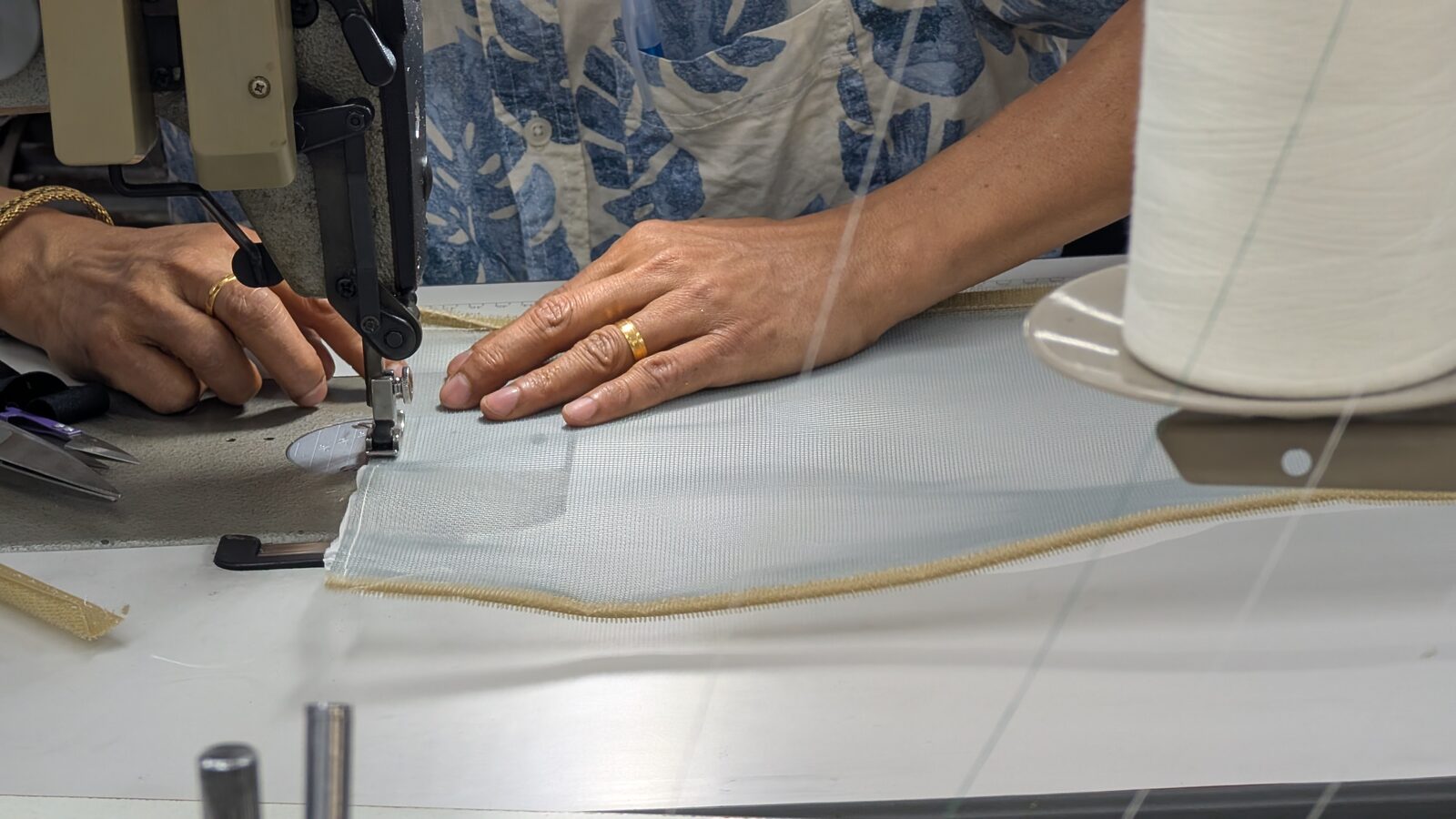 Hands guiding galvanized steel screen with Velcro trim through a sewing machine